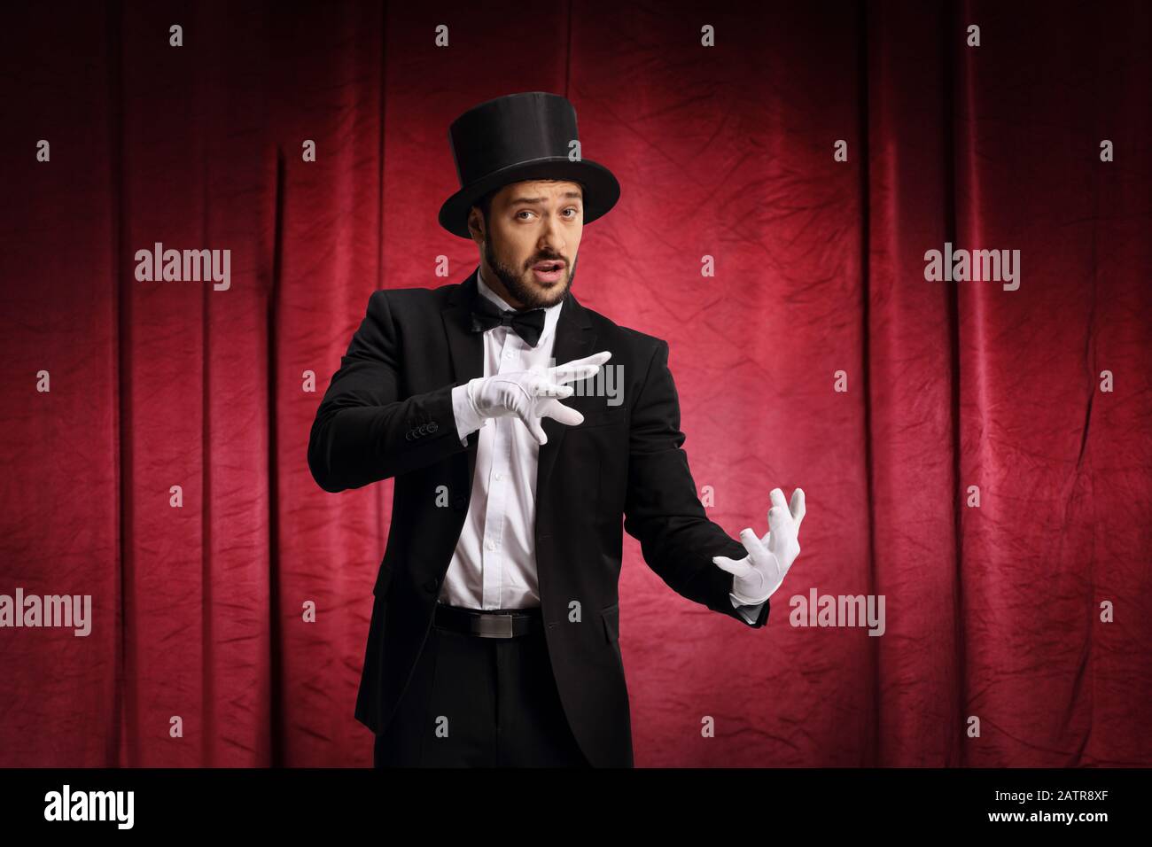 Männlicher Zauberer führt einen Trick mit Hut auf einer Bühne mit rotem Vorhang durch Stockfoto
