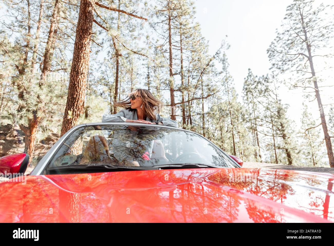 Junge, stilvolle Frau, die mit einem Cabriolet-Auto auf der Natur unterwegs ist, mit Blick aus dem Auto im Wald. Weitblick Stockfoto