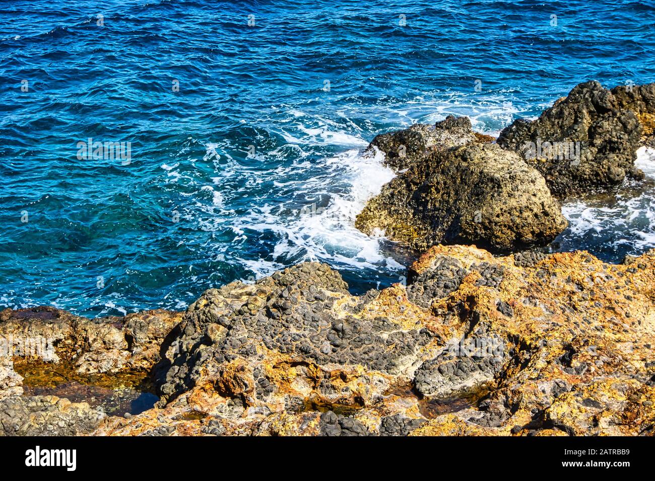 Horizontales Foto mit Details zu Felsen am Meeresufer in der Nähe der Inselhauptstadt Nisyros. Das Meer ist mit Wellen und Felsen bedeckt von orangefarbener Farbe, die durch verursacht wird Stockfoto
