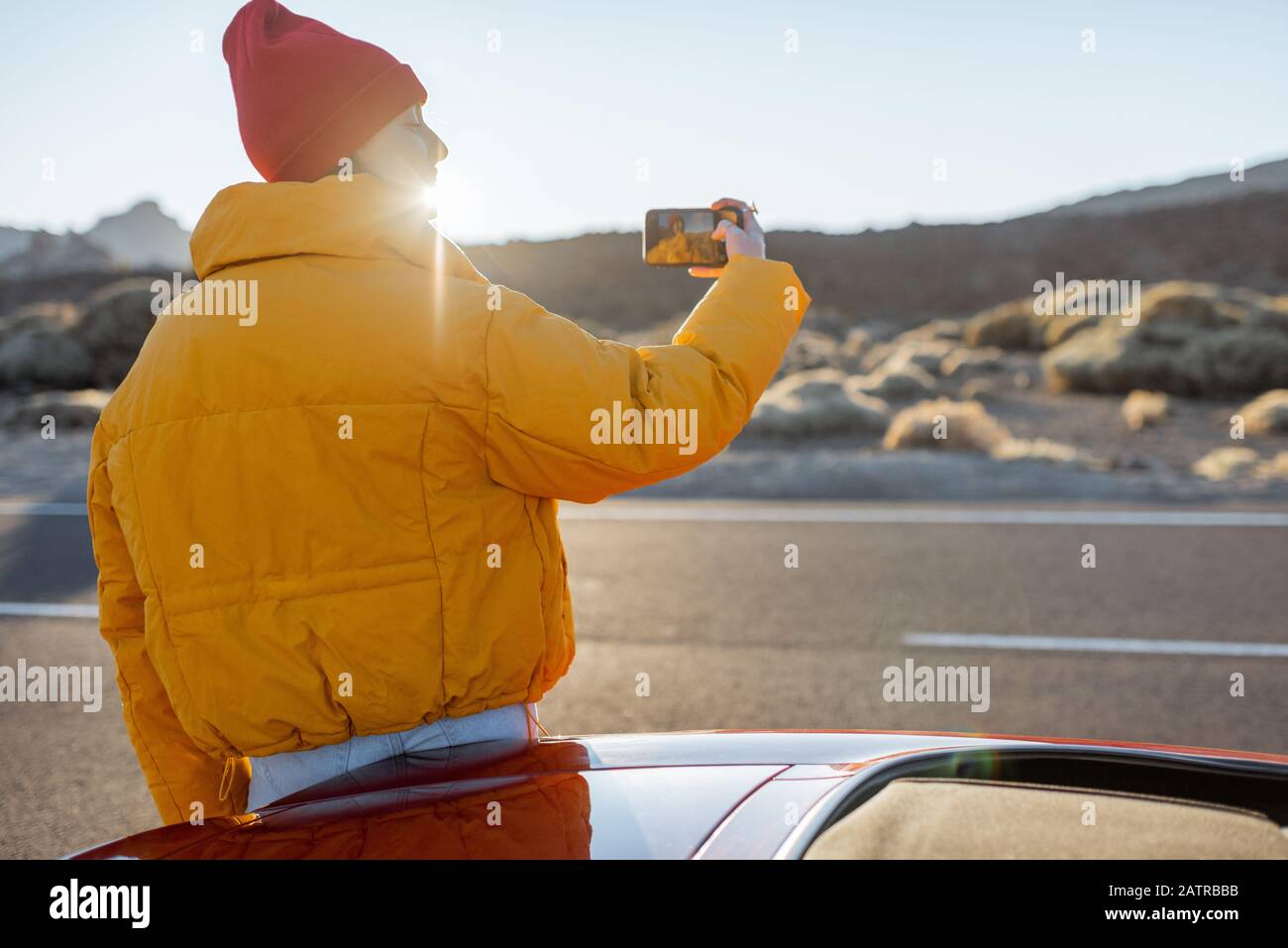 Frau, die wunderschöne vulkanische Landschaften genießt und während eines Sonnenuntergangs am Straßenrand telefoniert. Reisen im Wüstental auf Teneriffa Stockfoto