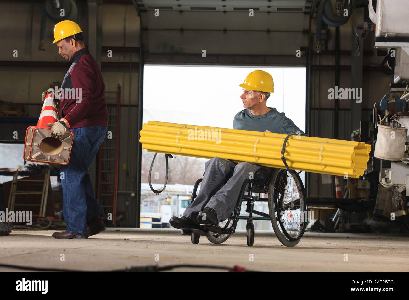 Behinderter Arbeiter und ein Kollege, der in einer Werkstatt Material umzieht Stockfoto
