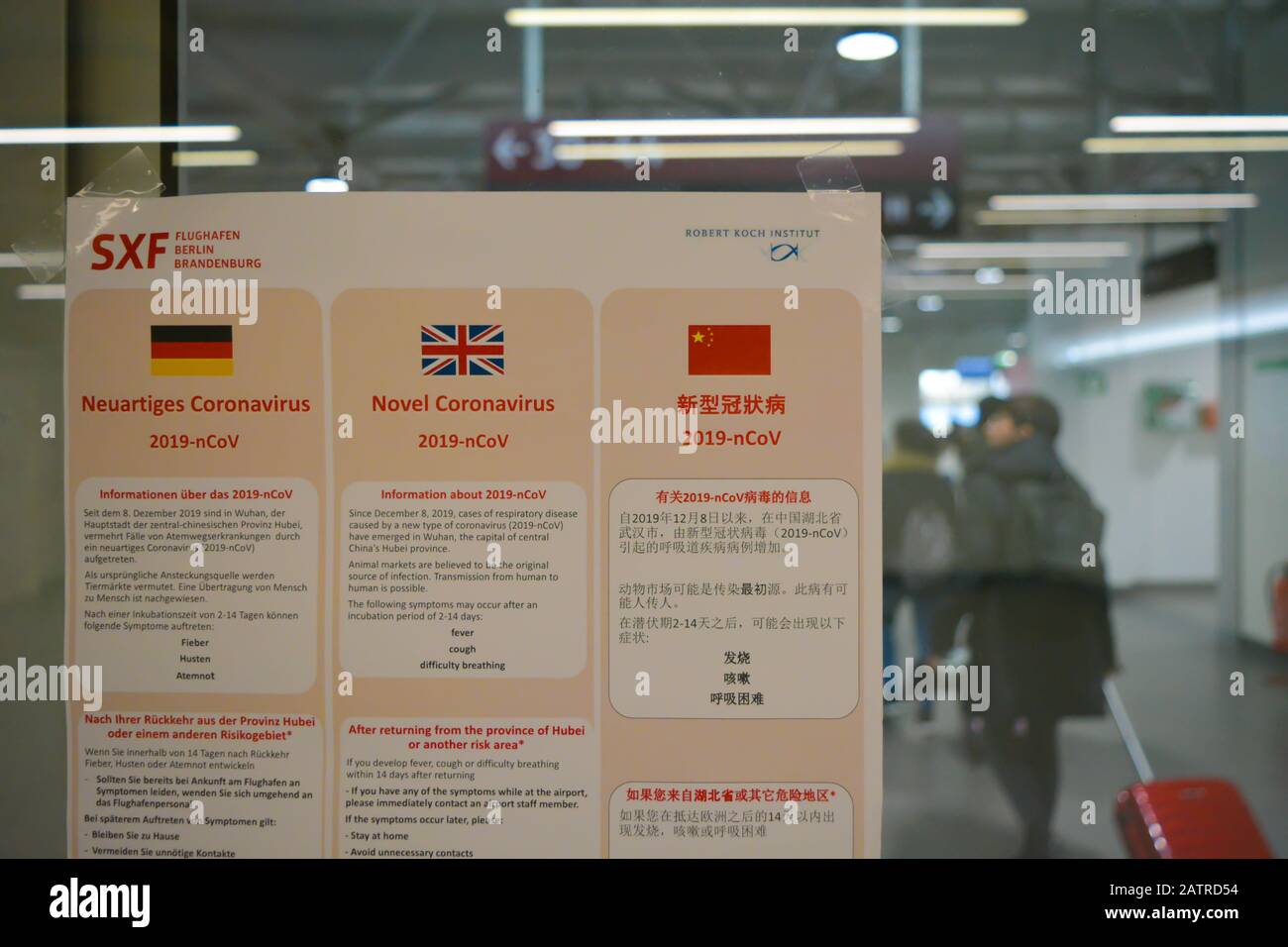 Warnschild Flughafen Berlin Schonefeld SXF, Deutschland berät alle Reisenden über Coronavirus 2019-nCoV. Chinesischer Tourist mit rotem Rollwagen in der Nähe Stockfoto