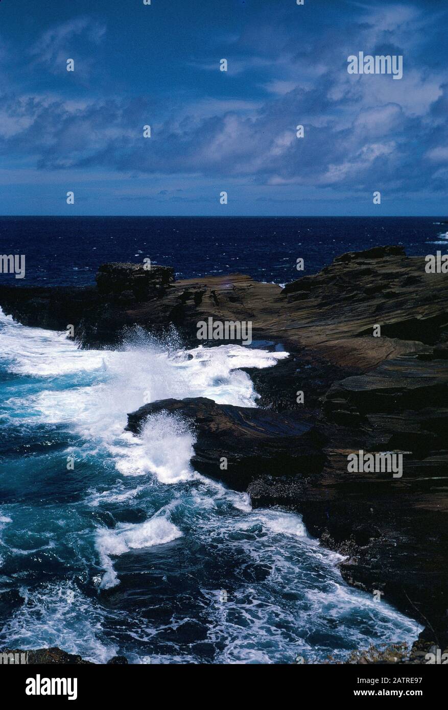 Nakuläres Foto, aufgenommen auf einer analogen 35-mm-Filmtransparenz, die vermutlich braune Felsbildung neben dem Körper des Wassers während des Tages, 1970, abbildet. Zu den wichtigsten Themen/Objekten gehören Meer, Ozean, Wasser, Felsen und Strand. () Stockfoto