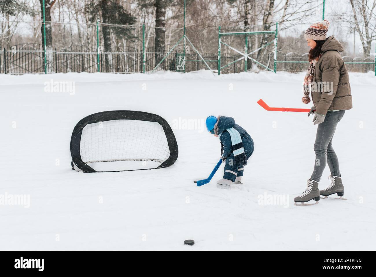 Kleiner lustiger Junge mit ihrer Mutter, die im Park Schlittschuhlaufen macht. Spielen Sie Eishockey mit Stick und Tor. Im Freien. Wintersport Stockfoto