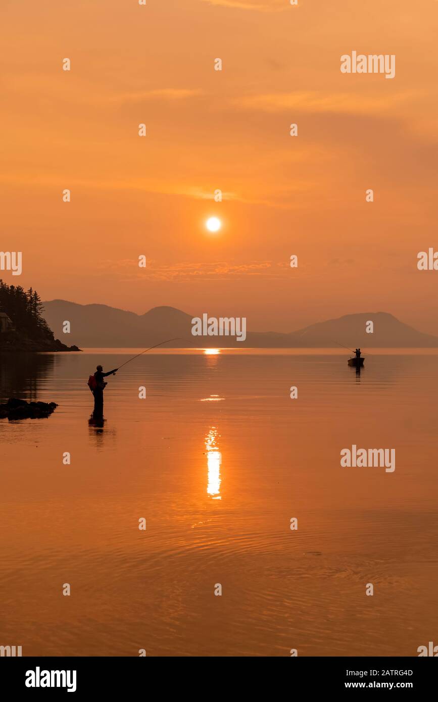 Silhouetted Angler im ruhigen Wasser stehend Angeln für König Lachs in der Dämmerung; Alaska, Vereinigte Staaten von Amerika Stockfoto