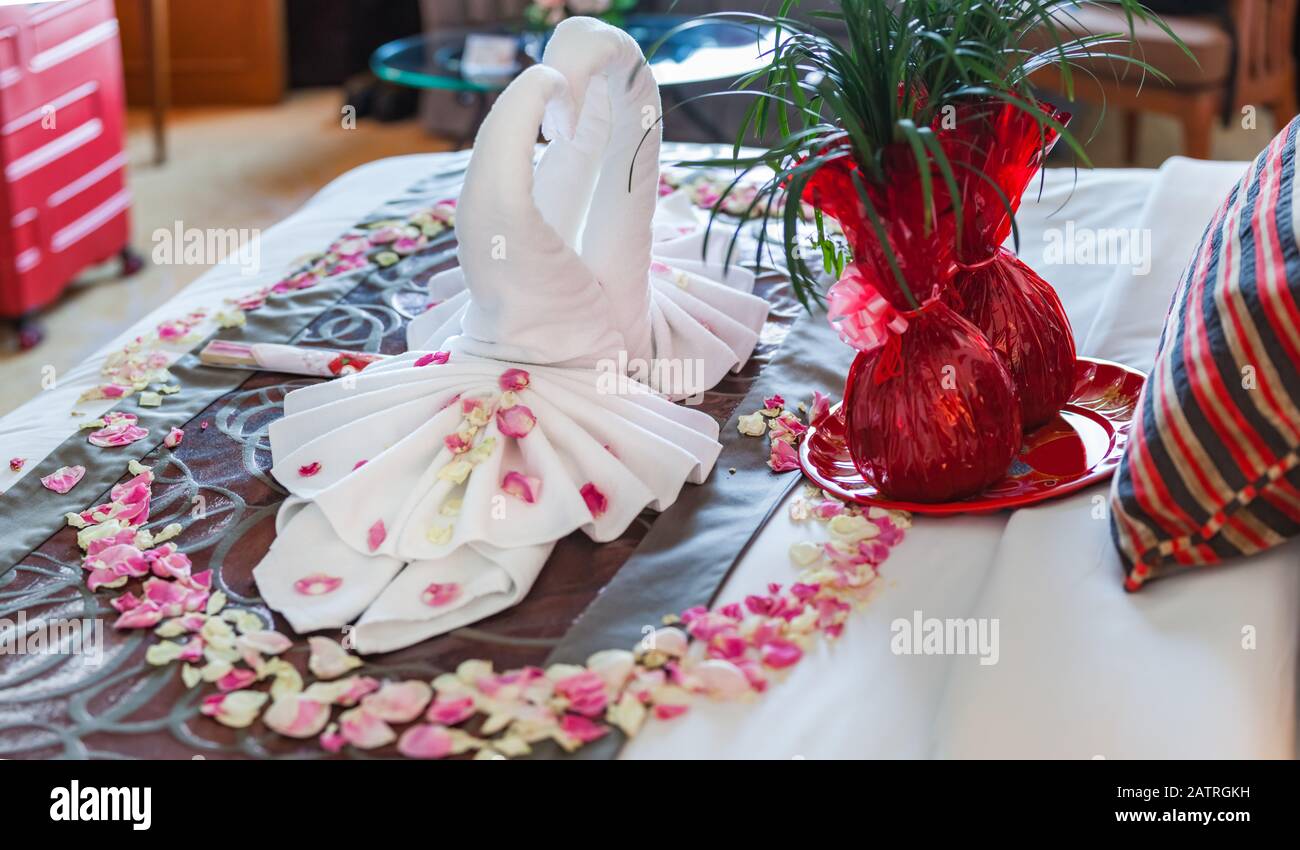 Romantisches Schlafzimmer Innenraum, Küssen Swan Origami Handtücher und streute frische Rosa Weiße Rose Blumenblätter Dekoration auf dem Bett für frisch verheiratete Paare. Weddin Stockfoto