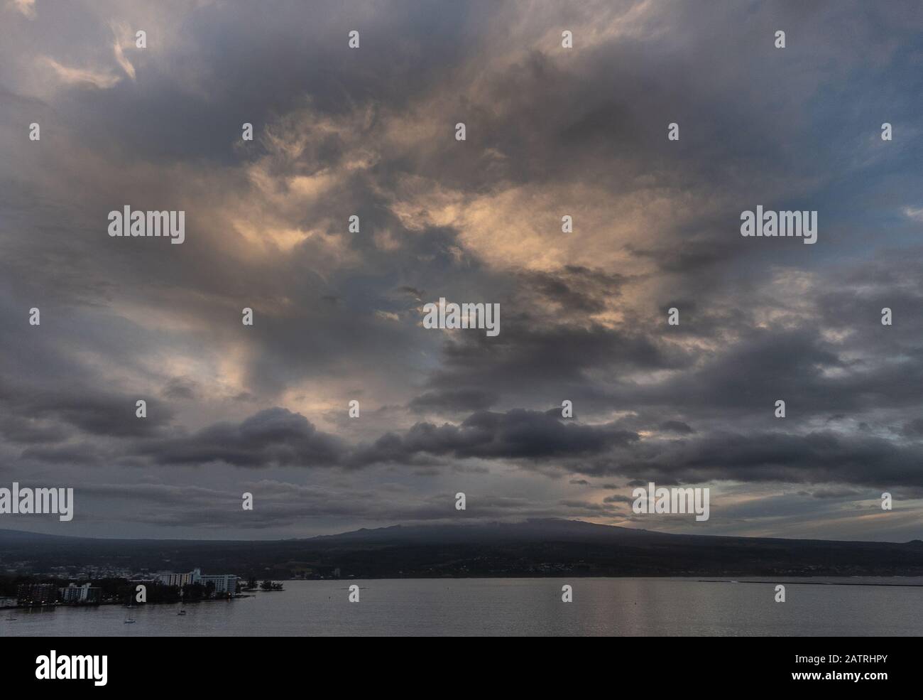 Hilo, Hawaii, USA. - 14. Januar 2020: Spektakuläre dunkle Abendwolkenlandschaft mit gelben Sonnenflecken über Stadt und Vulkan am Horizont. Stockfoto
