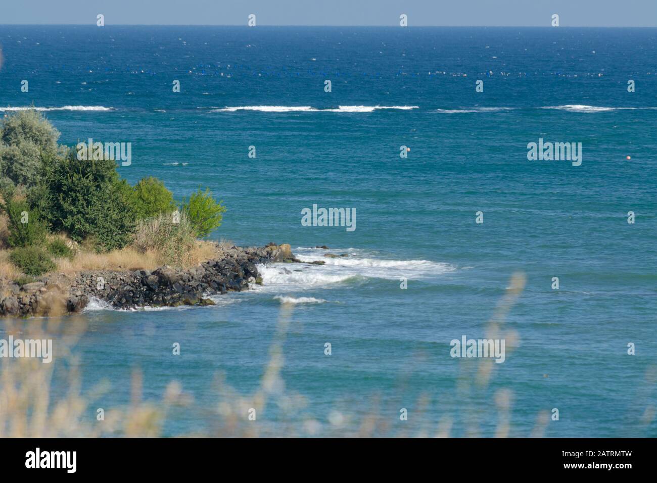 Meeresküste von der Klippe durch das wachsende Gras. Bucht in blauem, wunderschönem Meer mit kleinen weißen Wellen mitten im Tag. Steinufer mit GREE Stockfoto