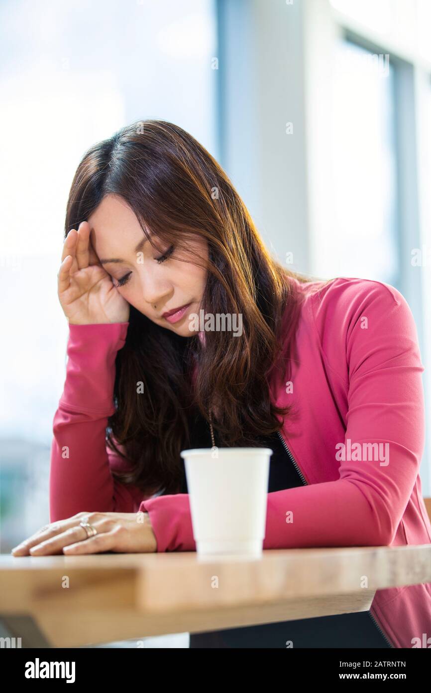 Eine professionelle asiatische Geschäftsfrau, die sich völlig überwältigt und traurig fühlt, während sie eine Pause in einem Café an ihrem... Stockfoto