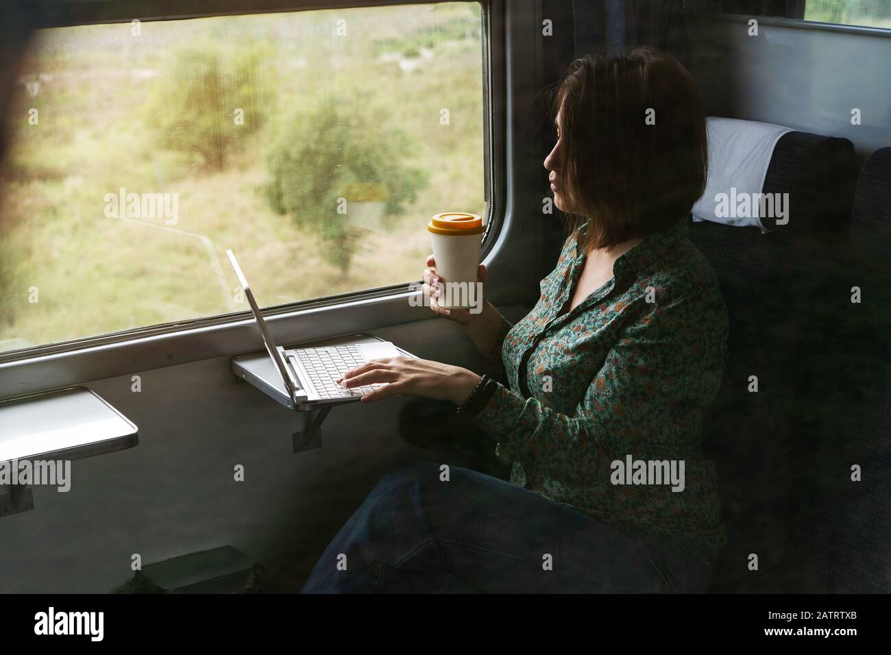 Eine Frau sitzt am Fenster einer S-Bahn mit einem Laptop und Kaffee Tasse Stockfoto