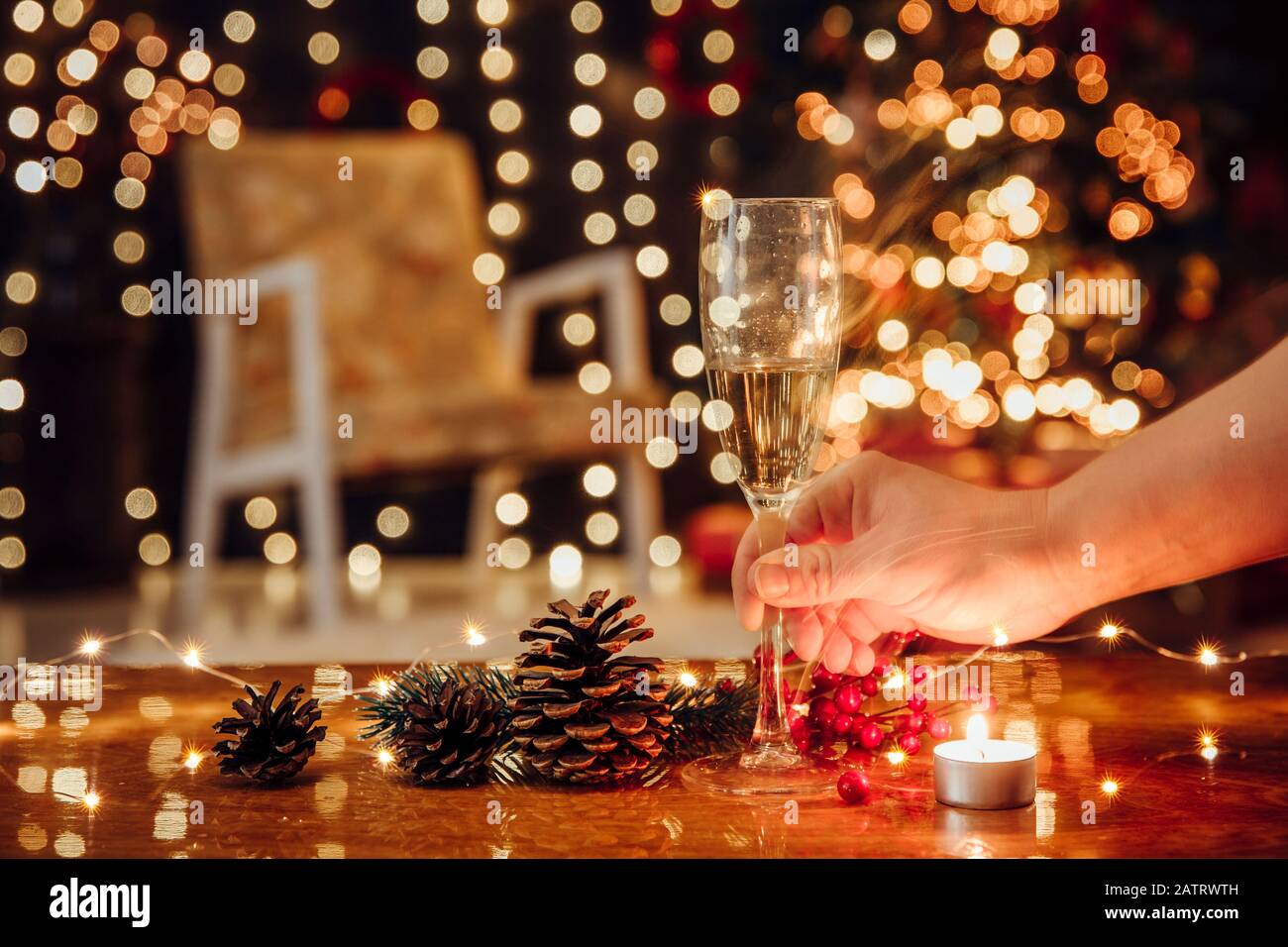 Weihnachtsfeiertage allein verbringen und Champagner allein trinken, Weihnachtsdepression und Alkoholismuskonzept. Selektive Fokussierung auf die Hand mit Alkoholflöte Stockfoto