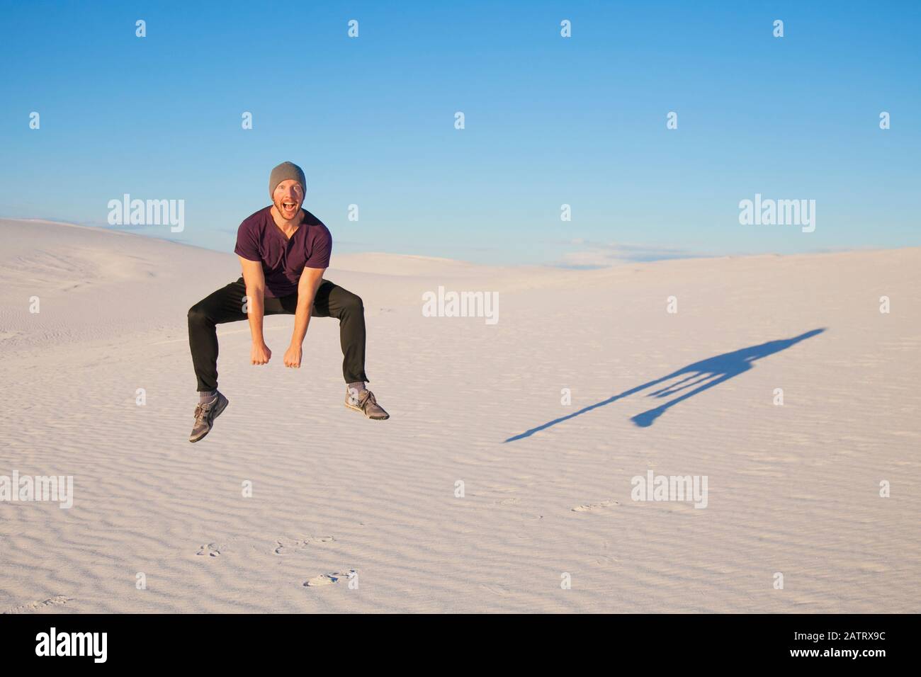 Unbeschwerter Mann in der Luft auf dem weißen Sand mit blauem Himmel, werfen einen Schatten neben ihm, White Sands National Monument Stockfoto