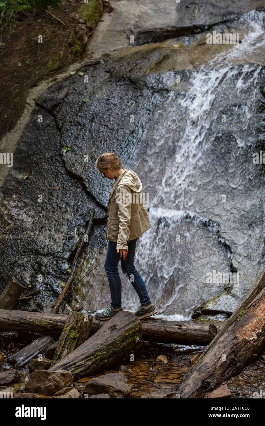 Ein Mädchen aus der Vorstufe gleicht sich aus, während es auf einem Baumstamm vor einem Wasserfall läuft; Lachsarm, British Columbia, Kanada Stockfoto