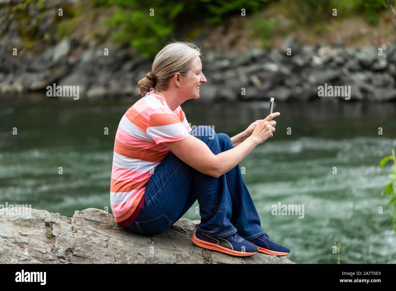 Frau, die auf einem Felsen am Rande des Adams River sitzt und mit einem Smartphone fotografiert; Lachs Arm, British Columbia, Kanada Stockfoto