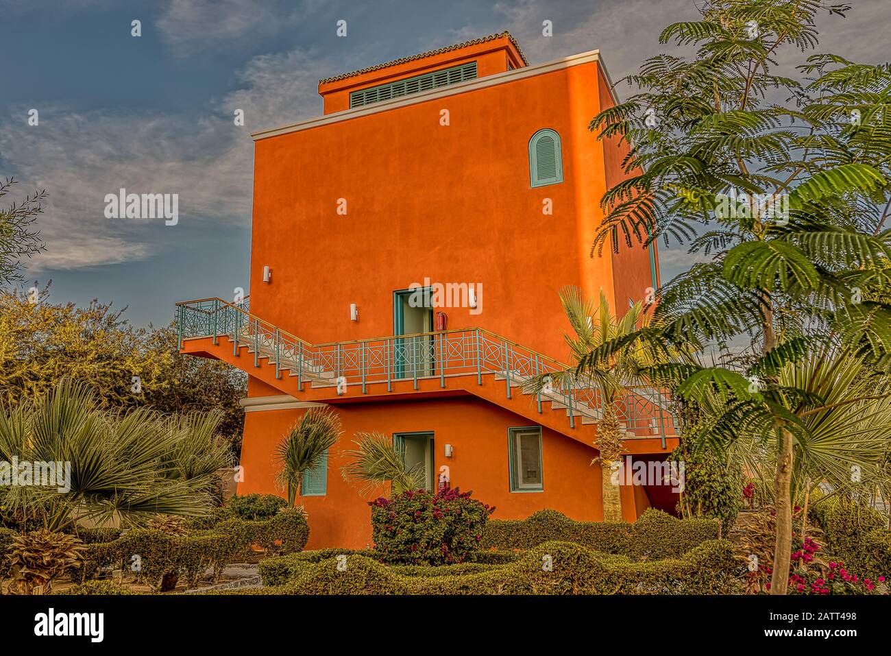 Ein viereckiges rotes ockergezungtes Haus unter den Palmen im Sonnenschein gegen einen blauen Himmel, El Gouna, Ägypten, 12. Januar 2020 Stockfoto