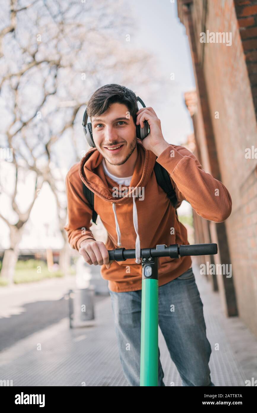 Porträt des jungen lateinmannes, der auf der Straße der Stadt einen Elektroscooter fährt. Modernes und ökologisches Transportkonzept. Stockfoto