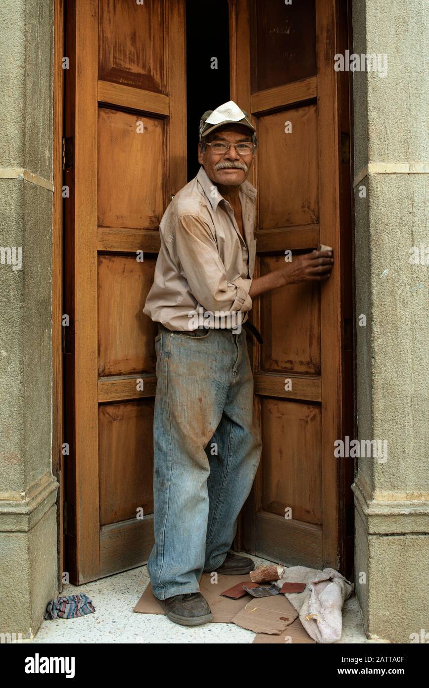 Umweltporträt eines älteren Tischlers bei der Arbeit, Holztür manuell schleifen. Alltag in Antigua, Guatemala. Januar 2019 Stockfoto
