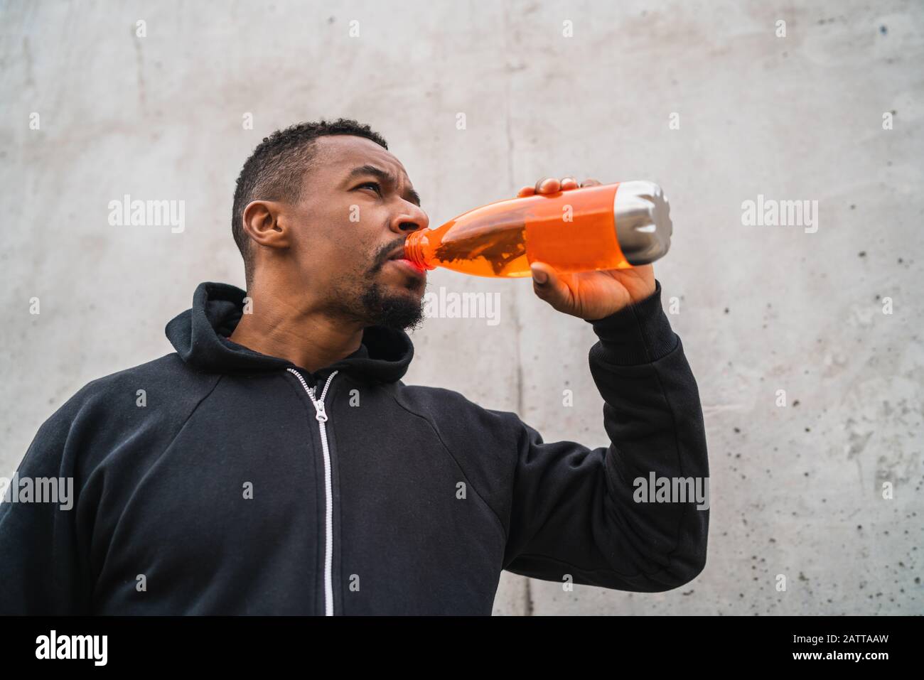 Portrait eines athletischen Mannes, der etwas getrunken hat, nachdem er vor grauem Hintergrund trainiert hatte. Sport und Gesundheit. Stockfoto