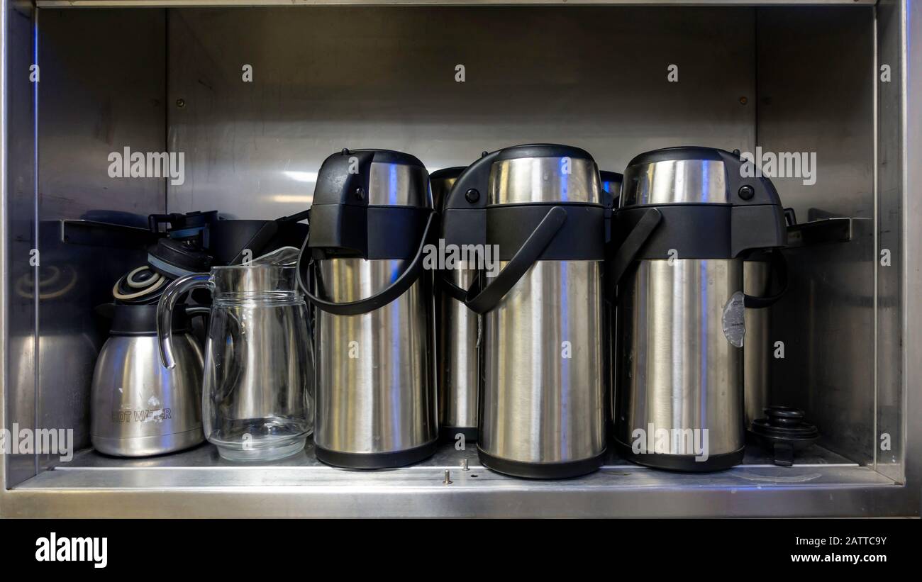 Alt ein schmutzig aussehender Heißwasserkolben in einem alten Edelstahlschrank mit einer Glaskanne Stockfoto