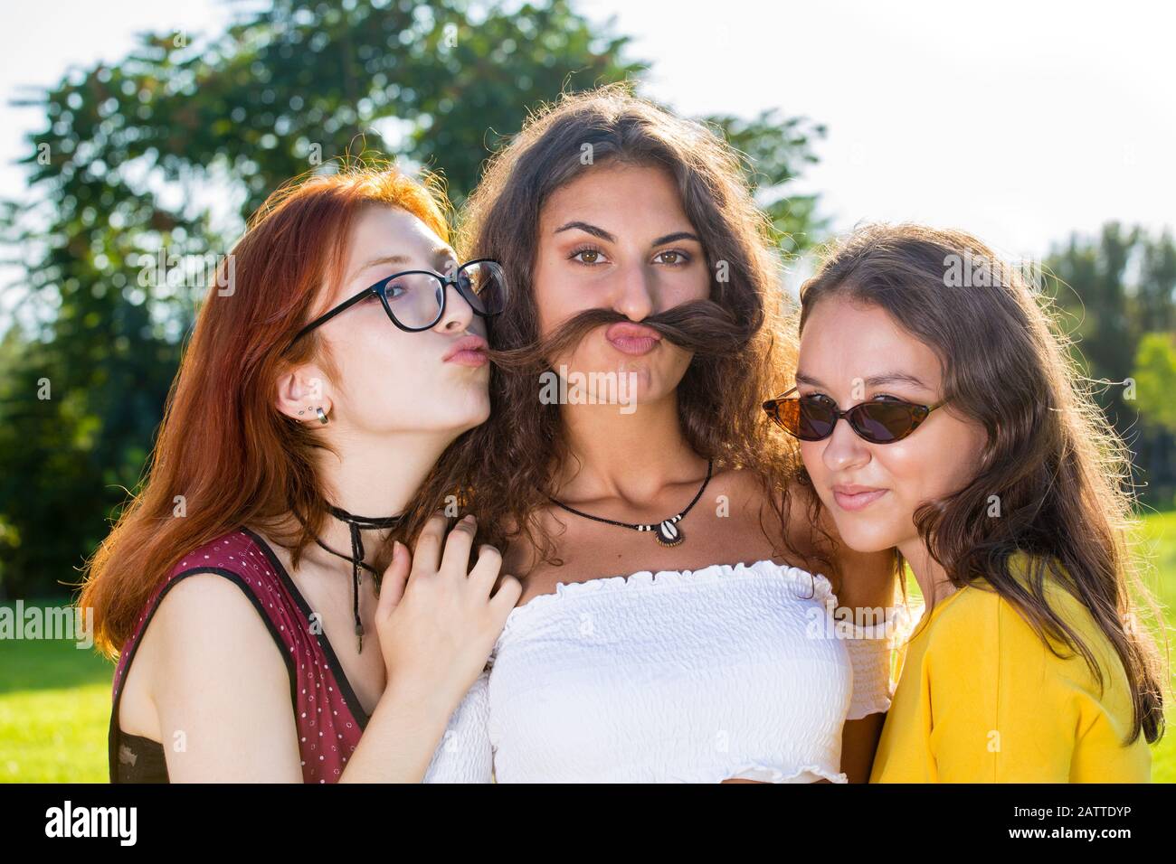 Schönes junges Mädchen mit ihren beiden Freunden, lustige Nahaufnahmen im Park, Kamera und Grimassen anblickend, wobei sie ihr Haar als Schnurrbart halten. Stockfoto