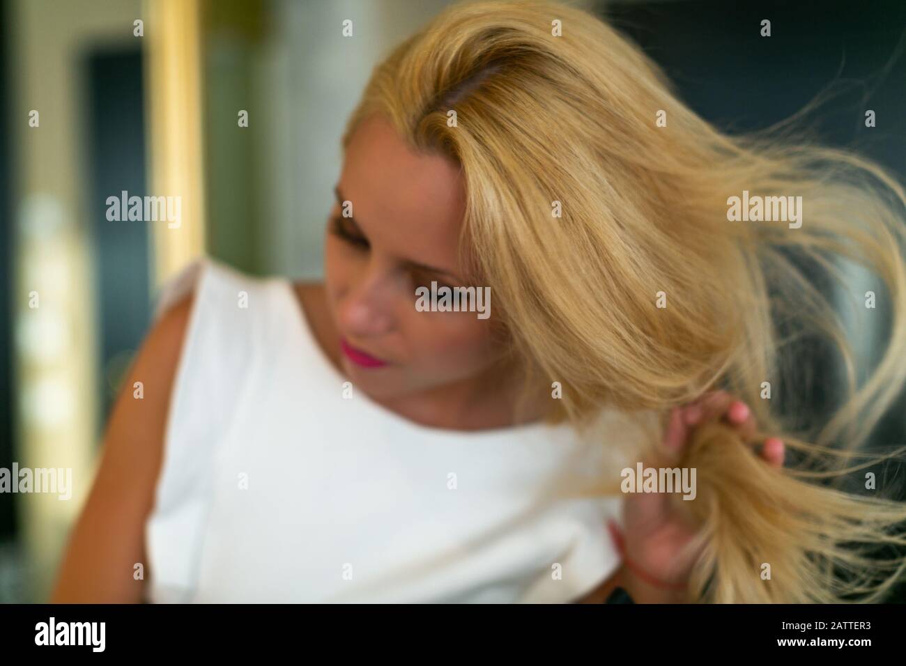 Mädchen berührt ihr blondes Haar, verschwommenes Foto mit einem Fokus auf die Haare des Models. Stockfoto