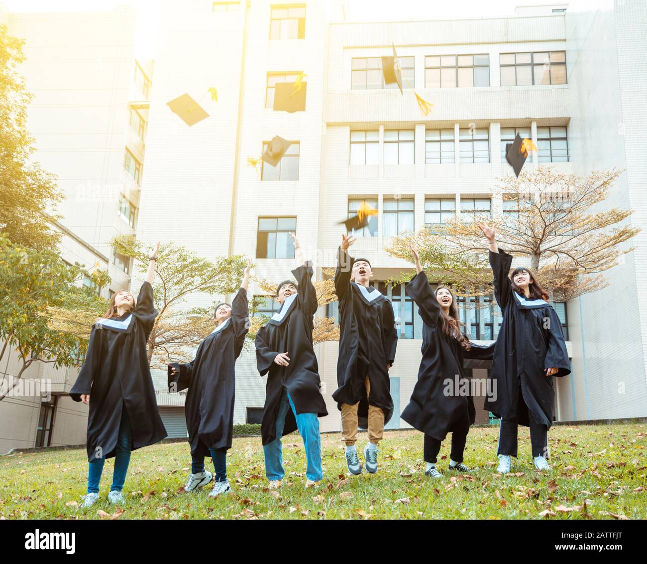 Fröhliche Studenten in Abschlussfeiern und Springen auf dem Campus der Universität Stockfoto