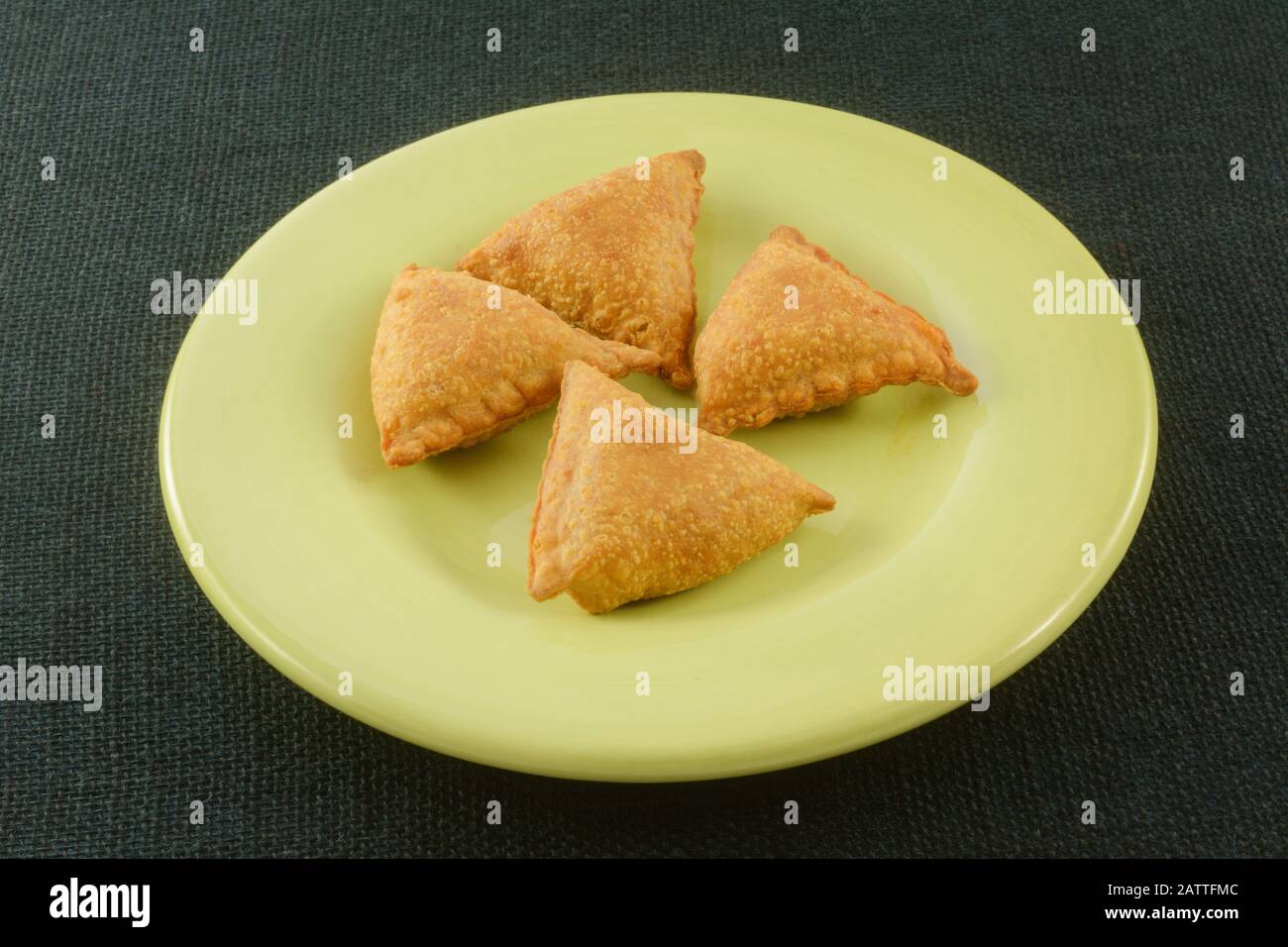 Warme, gekochte Samosa-Gebäck-Snacks oder Vorspeisen auf hellgrünem Teller auf dunkelgrünem Hintergrund Stockfoto