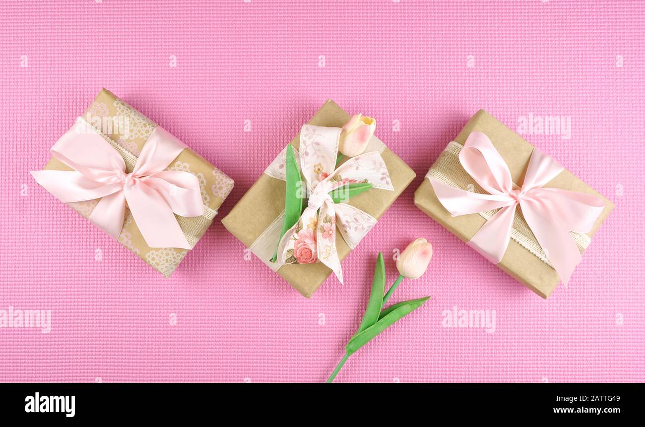 Geschenke, die in Kraftpapier und pinkfarbenen Bändern gewickelt sind, lagen in der Wohnung für Muttertag, Geburtstag oder Valentinstag. Negativer Kopierbereich. Stockfoto