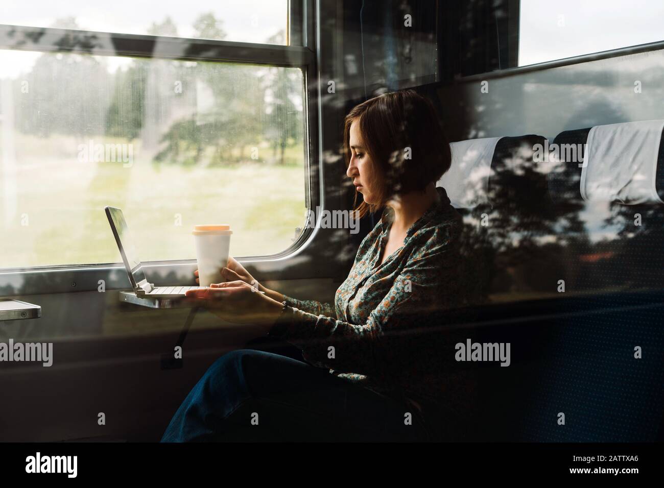 Eine Frau sitzt am Fenster einer S-Bahn mit einem Laptop und Kaffee Tasse Stockfoto