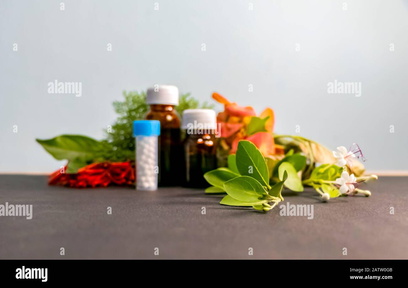 Homöopathisches Konzept - Verschwommenes Bild von Homöopathieflaschen mit weißen, roten, orangefarbenen Blumen und grünen Blättern Stockfoto