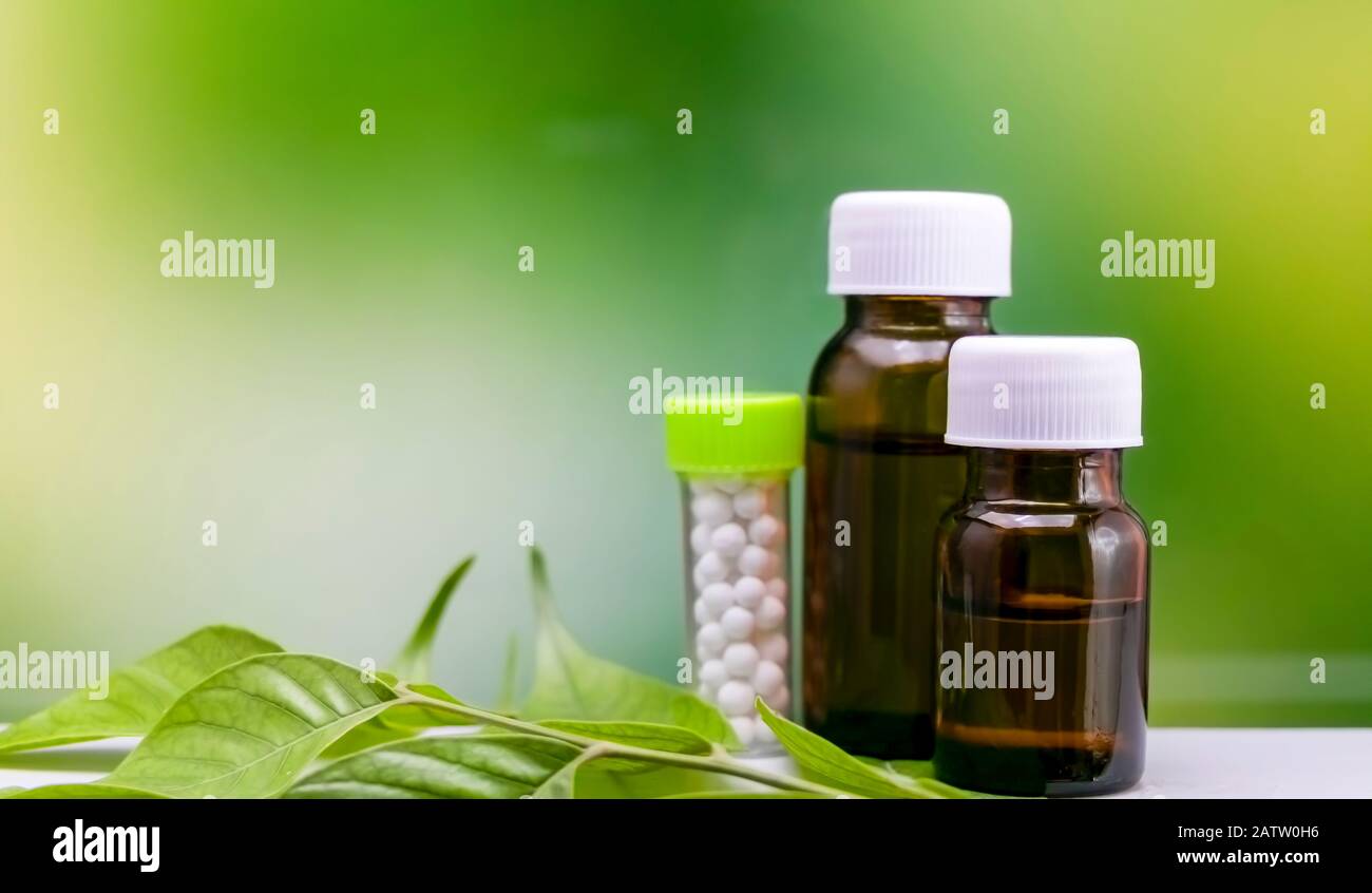 Homöopathie-Konzept - Drei Flaschen Homöopathie-Substanz auf grünem Blatt mit gemischtem gelbgrünem Hintergrund Stockfoto