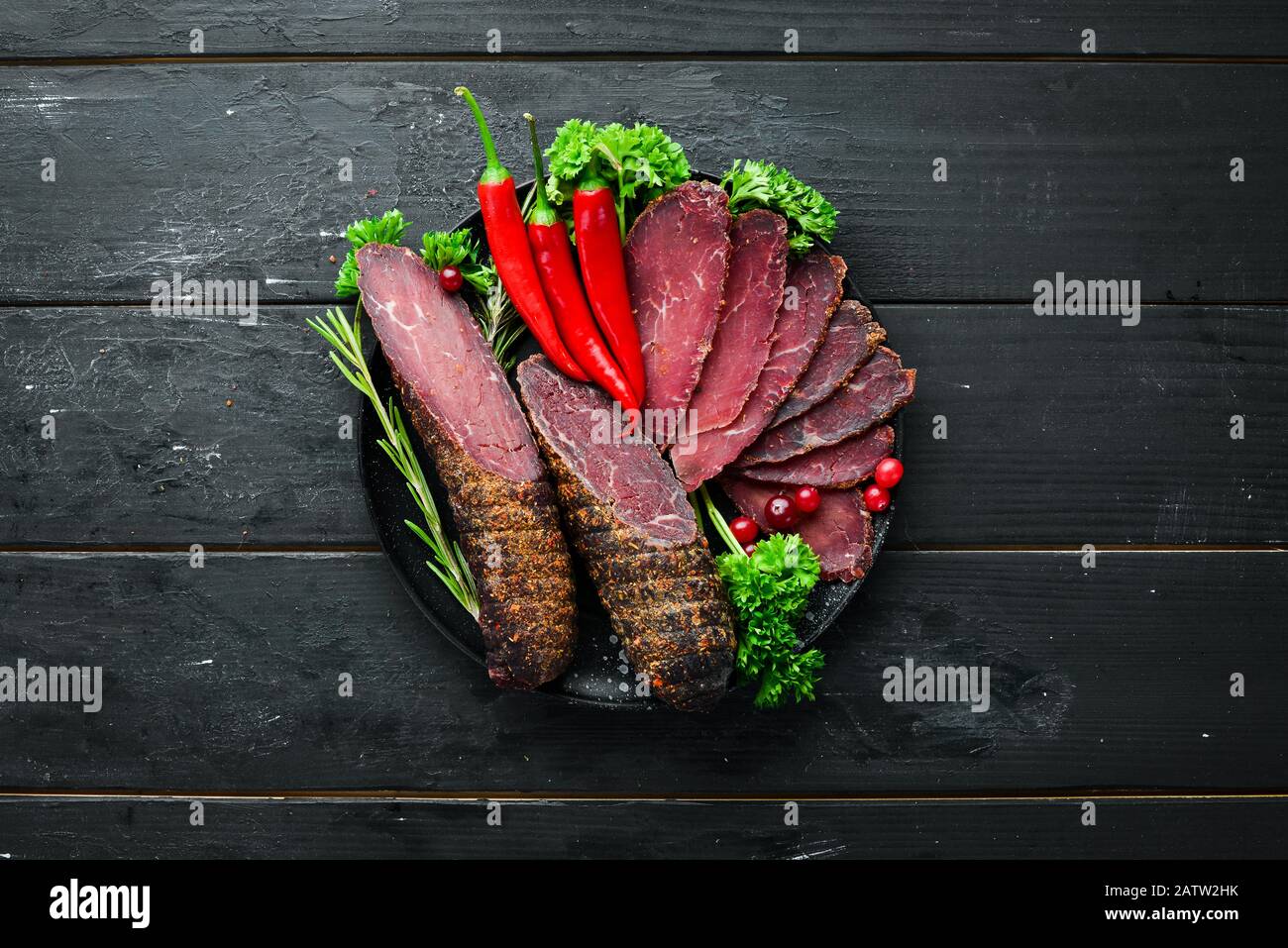 Getrocknetes Kalbsfleisch mit Gewürzen und Kräutern. Rindfleisch auf altem schwarzen Tisch ruckartig. Draufsicht. Freier Speicherplatz für Ihren Text. Stockfoto