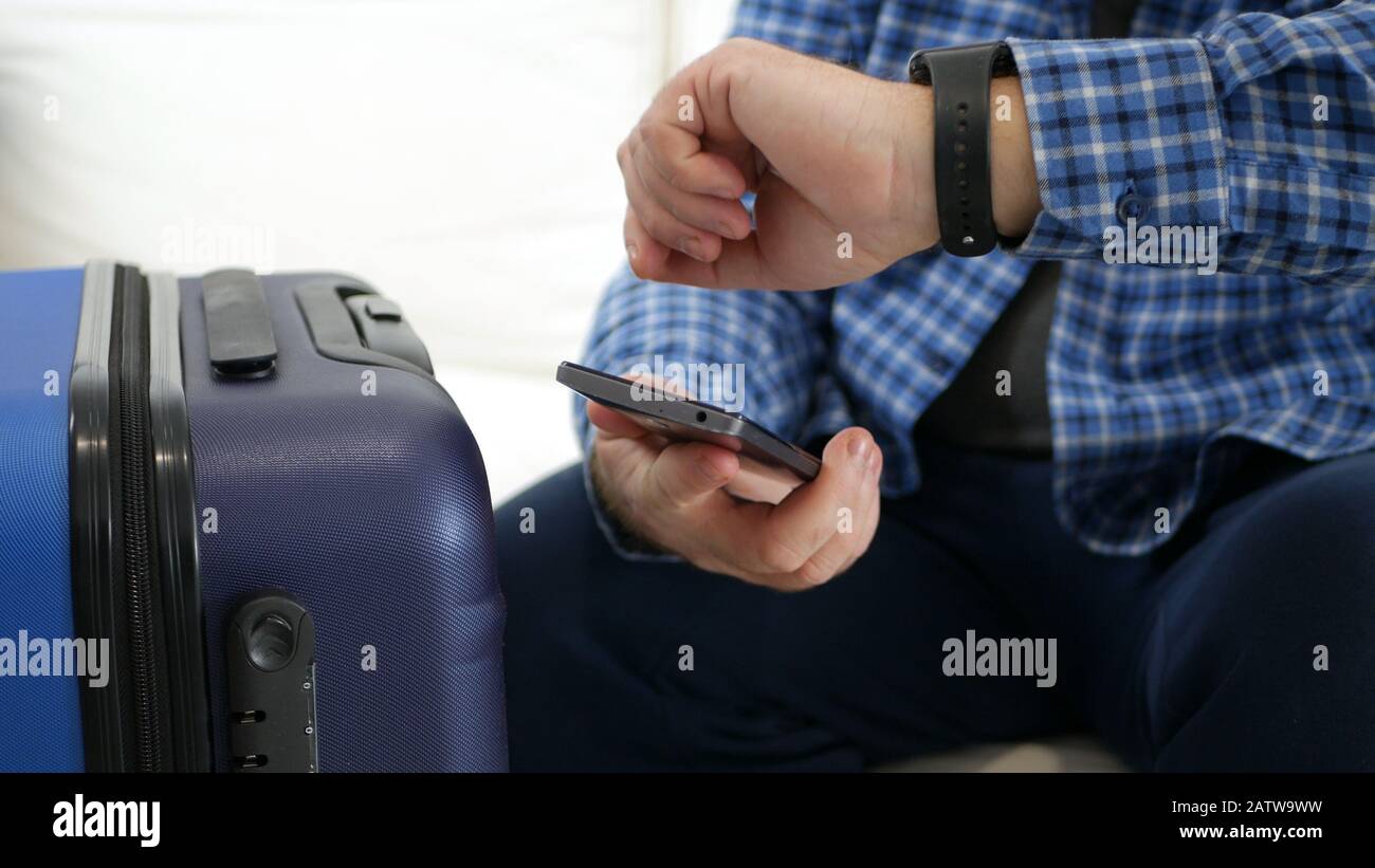 Mann mit Koffer Warten Transport Kontrollzeit auf Der Hand Uhr und Text Über Handy Stockfoto