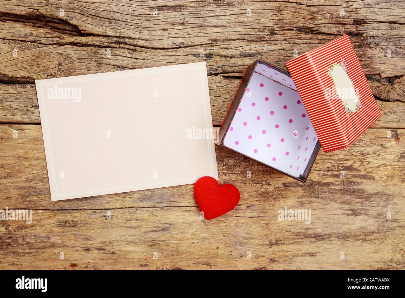 Unbeschriftete pinkfarbene Grußkarte mit Rahmen und leerem roten Geschenkkasten mit offener Abdeckung, mit rotem Herz auf Holzhintergrund verziert Stockfoto