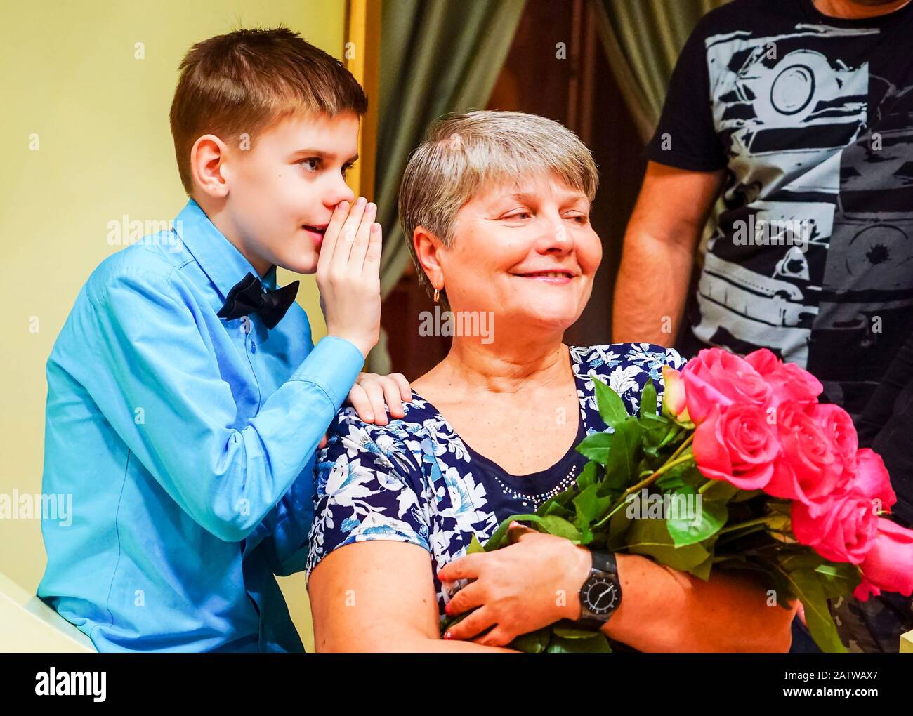 Der Junge flüstert im Ohr seiner Großmutter und teilt die Nachricht Stockfoto