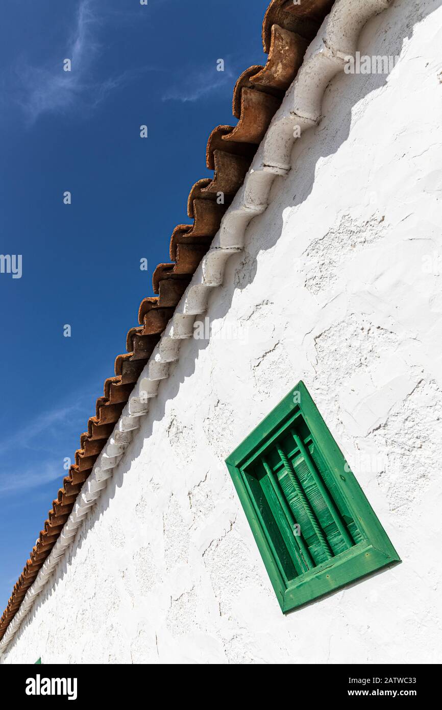 Abstraktes architektonisches Detail des grünen Fensters an einer weiß getünchten Wand mit Terrakotta-Ziegeldach gegen einen blauen Himmel auf einem restaurierten alten Bauernhaus, San Stockfoto