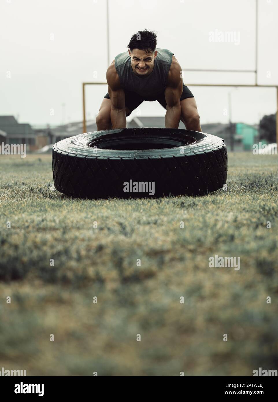 Starker junger Mann, der ein Flip-Workout für Reifen macht. Starker und muskulöser Athlet macht Cross-Training auf einem Feld. Stockfoto