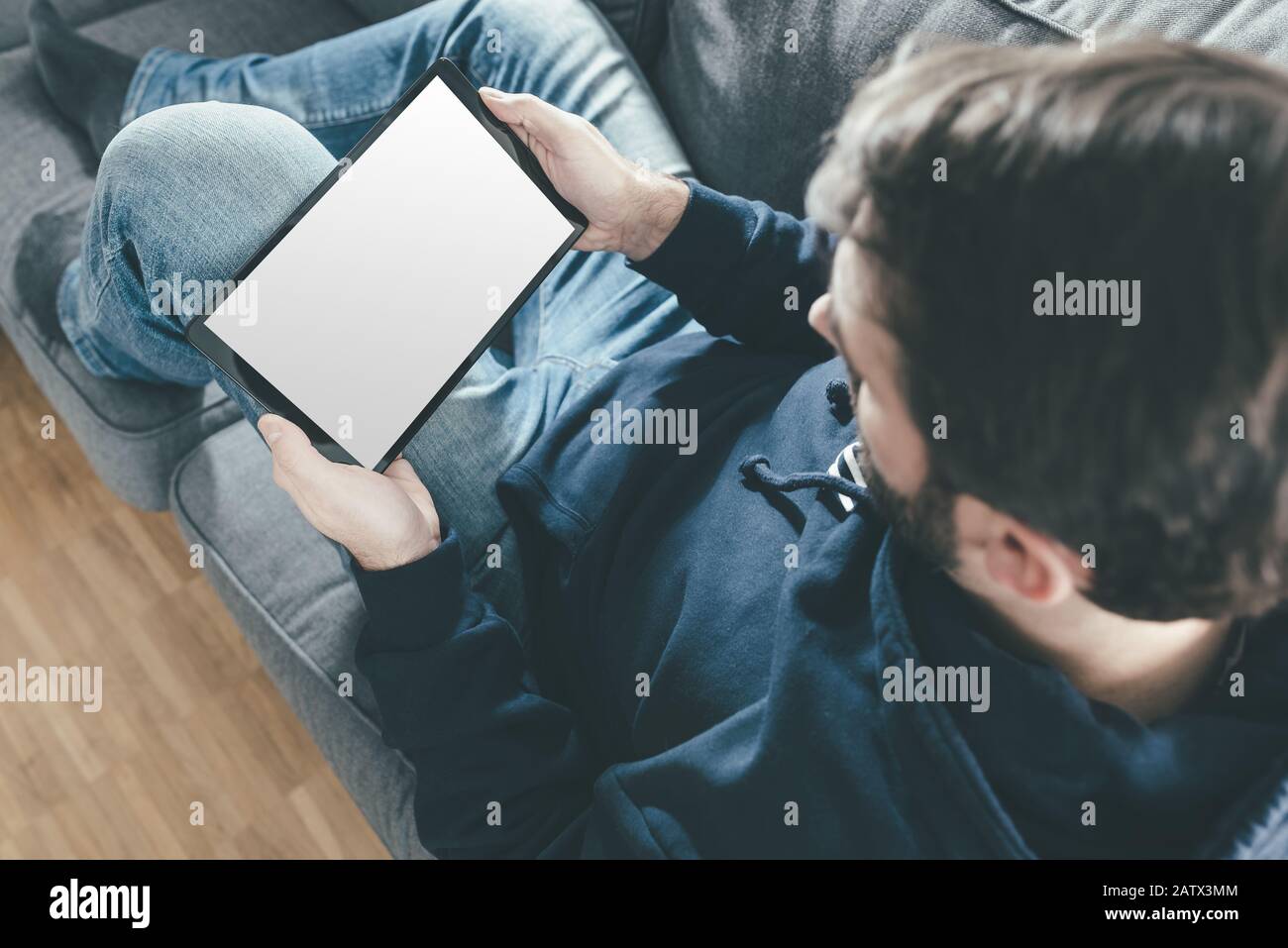 Hochwinkeliger Blick auf den Mann, der sich auf dem Sofa entspannt, während er einen Tablet-Computer verwendet Stockfoto