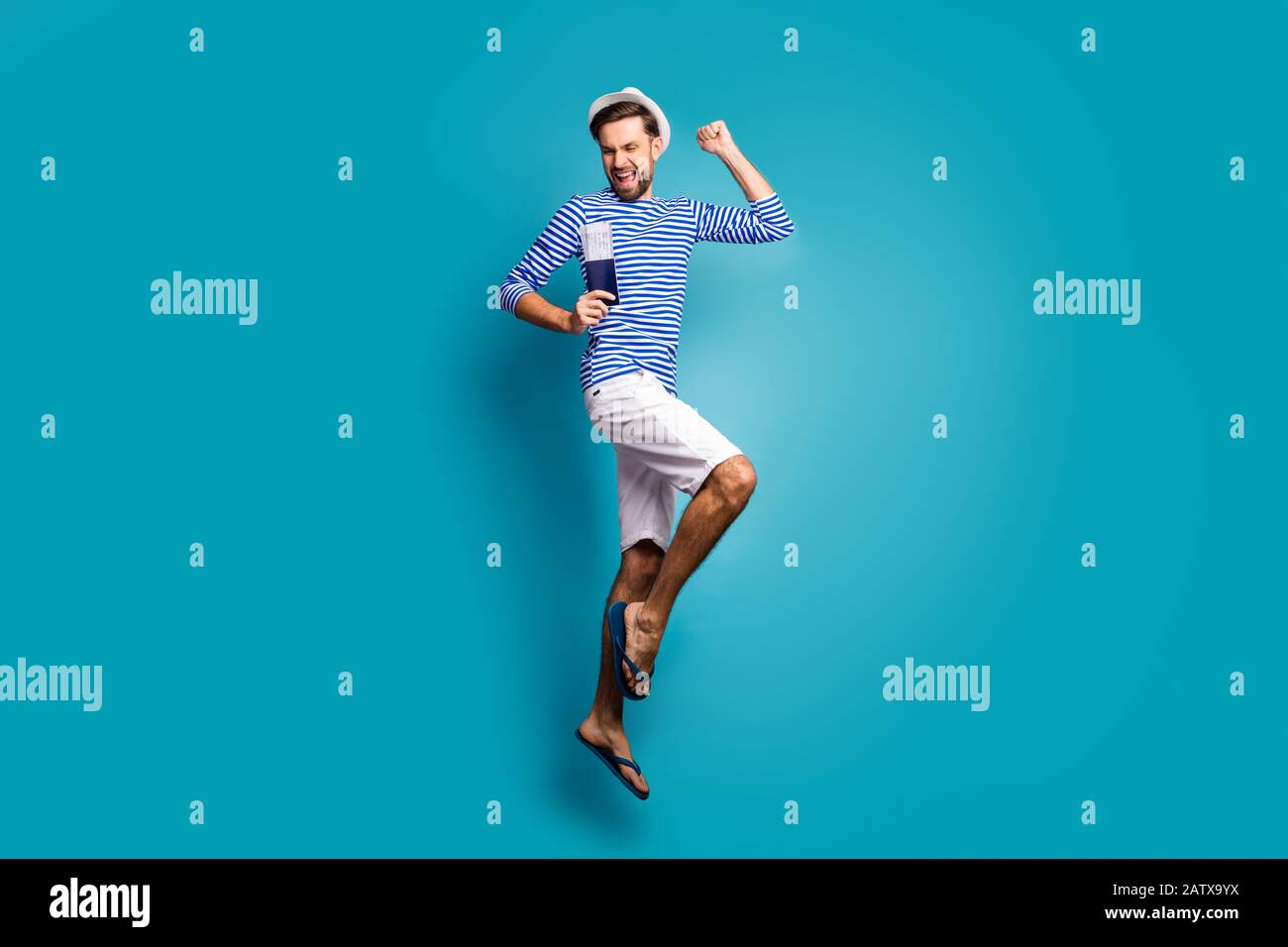 Lange Profilfoto von funky Kerl Tourist Jump hoch feiern Urlaub beginnen Visa-Mode gestreiftes Seemannshirt Weste Kappe Shorts Flip-Flops Stockfoto