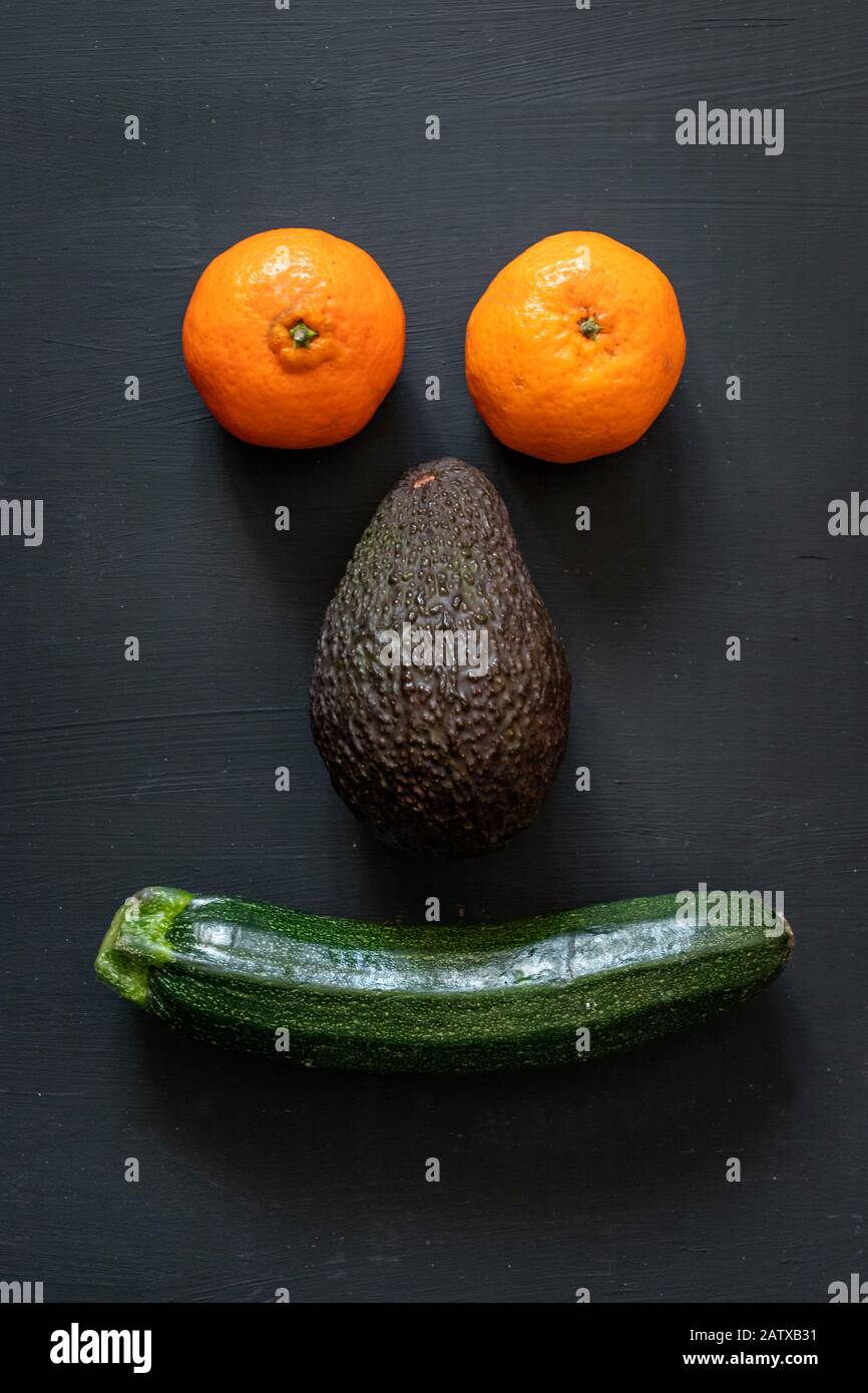 Orangen, Avocado und Zucchini Formen ein lächelndes Gesicht über einem dunklen Hintergrund Stockfoto