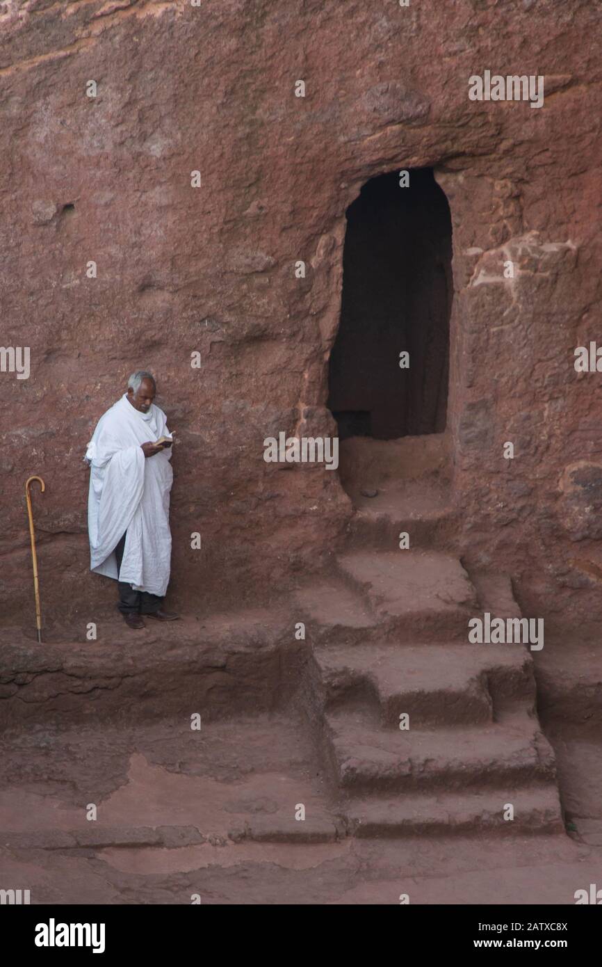 Lalibela, Äthiopien - Nov 2018: Menschen, die in weißer äthiopischer Kleidung verkleidet sind, beten neben der in Felsen ausgegrabenen Kirche in Lalibela. Stockfoto Lalibela, Äthiopien - Nov 2018: Menschen, die in weißer äthiopischer Kleidung verkleidet sind, beten neben der in Felsen ausgegrabenen Kirche in Lalibela. Stockfoto