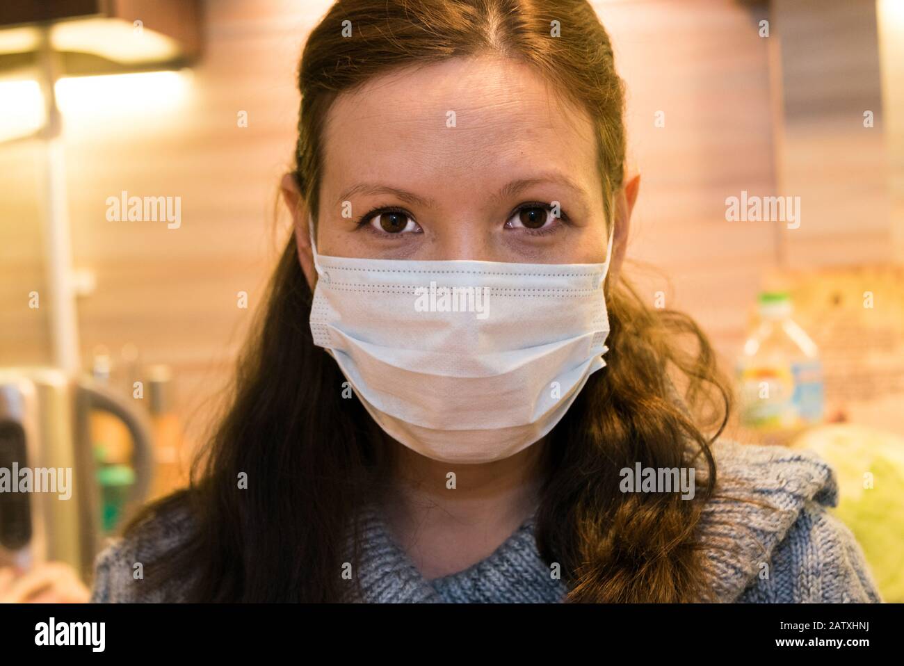 Frau in der Maske, die in der Küche an einer Grippe erkrankt ist. Stockfoto