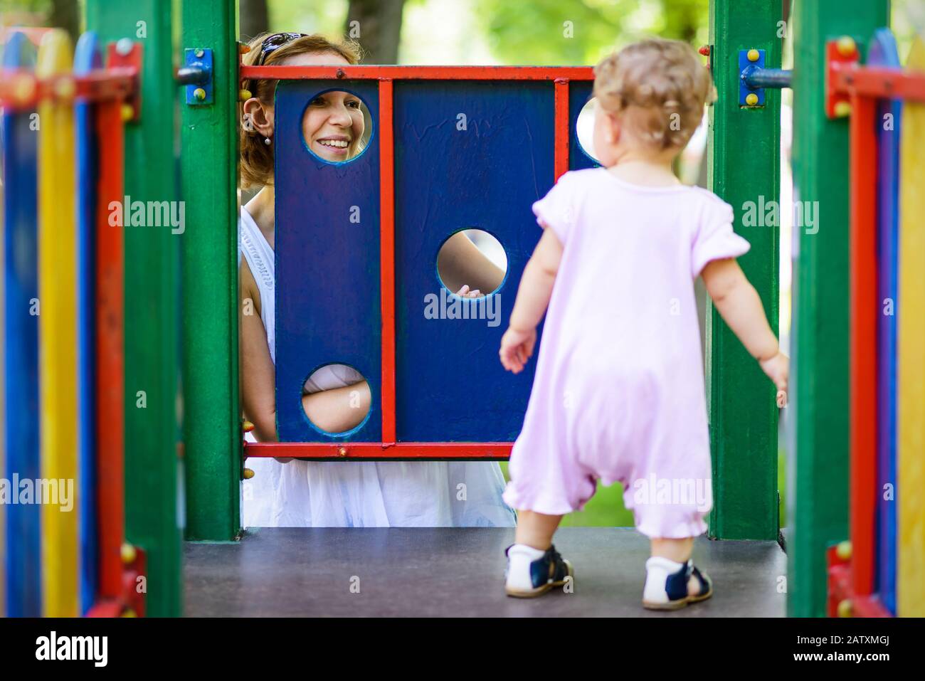 Fröhliche Mutter, die ihr kleines Mädchen auf dem Spielplatz betrachtet. Einjähriges Kind spielt mit der Mutter. Stockfoto