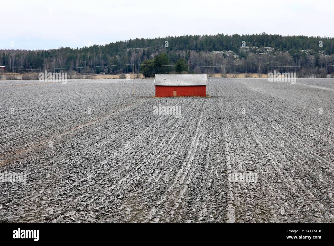 Rote Holzscheune in einem leicht schneebedeckten Feld an einem übergiebelten Wintertag. Sauvo, Finnland. Dezember 2019. Stockfoto