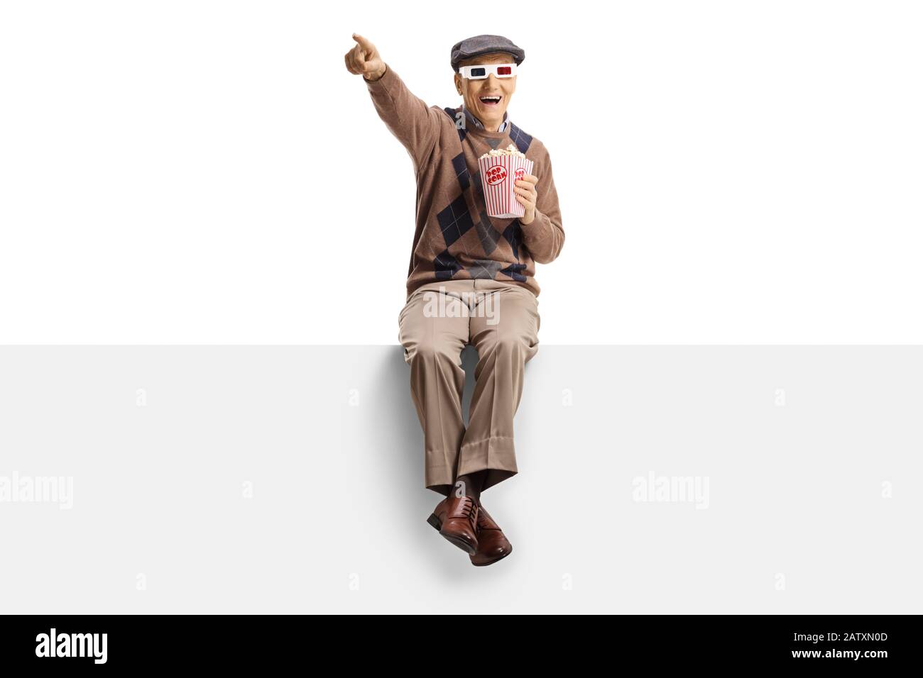Senior man mit 3D-Brille, die auf einem Panel sitzt und Popcorn isst, lacht und zeigt isoliert auf weißem Hintergrund Stockfoto
