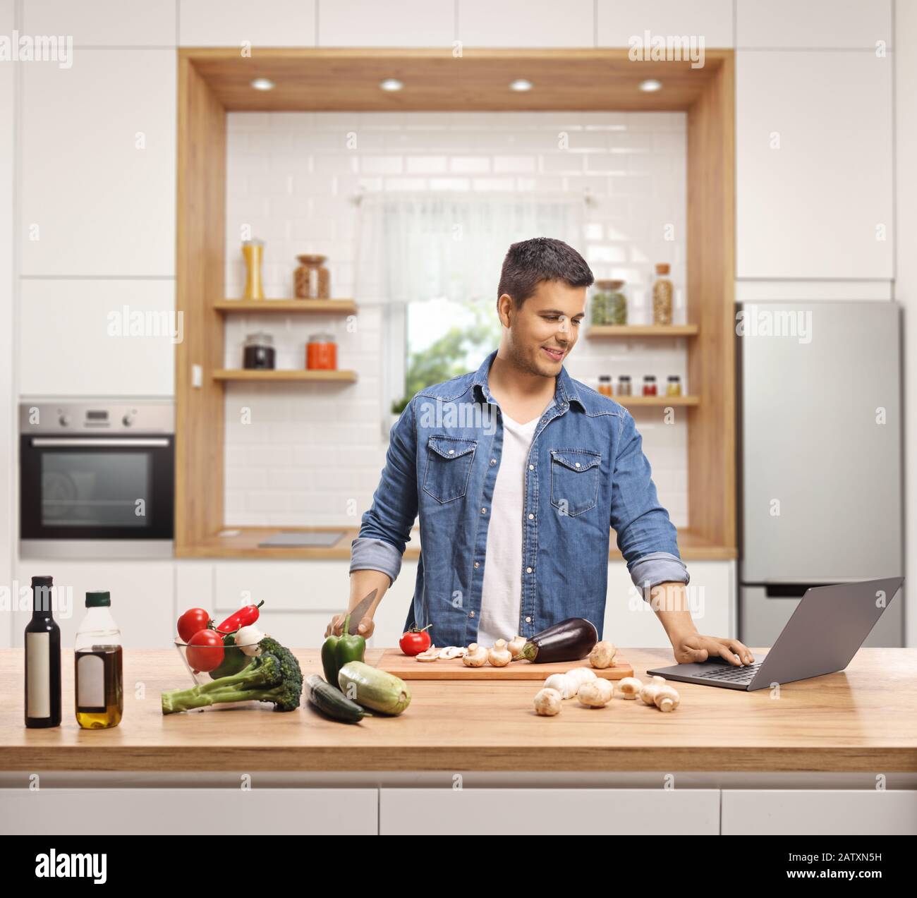 Junger Mann, der in einer Küche mit einem Laptop kocht Stockfoto