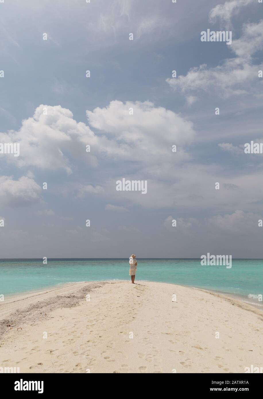 Konzept Reisen - Frau am Strand; EINE alleinstehende Frau, die an einem tropischen Strand mit weißem Sand, blauem Himmel und türkisfarbenem Wasser steht, Rückansicht, die Malediven, Asien Stockfoto