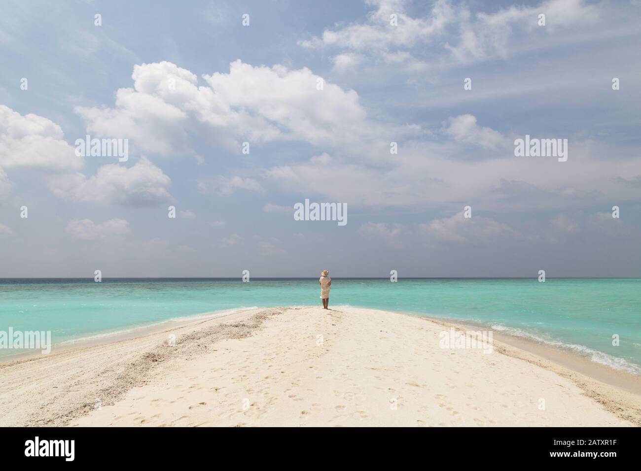Konzept Reisen - Frau am Strand; EINE alleinstehende Frau, die an einem tropischen Strand mit weißem Sand, blauem Himmel und türkisfarbenem Wasser steht, Rückansicht, die Malediven, Asien Stockfoto