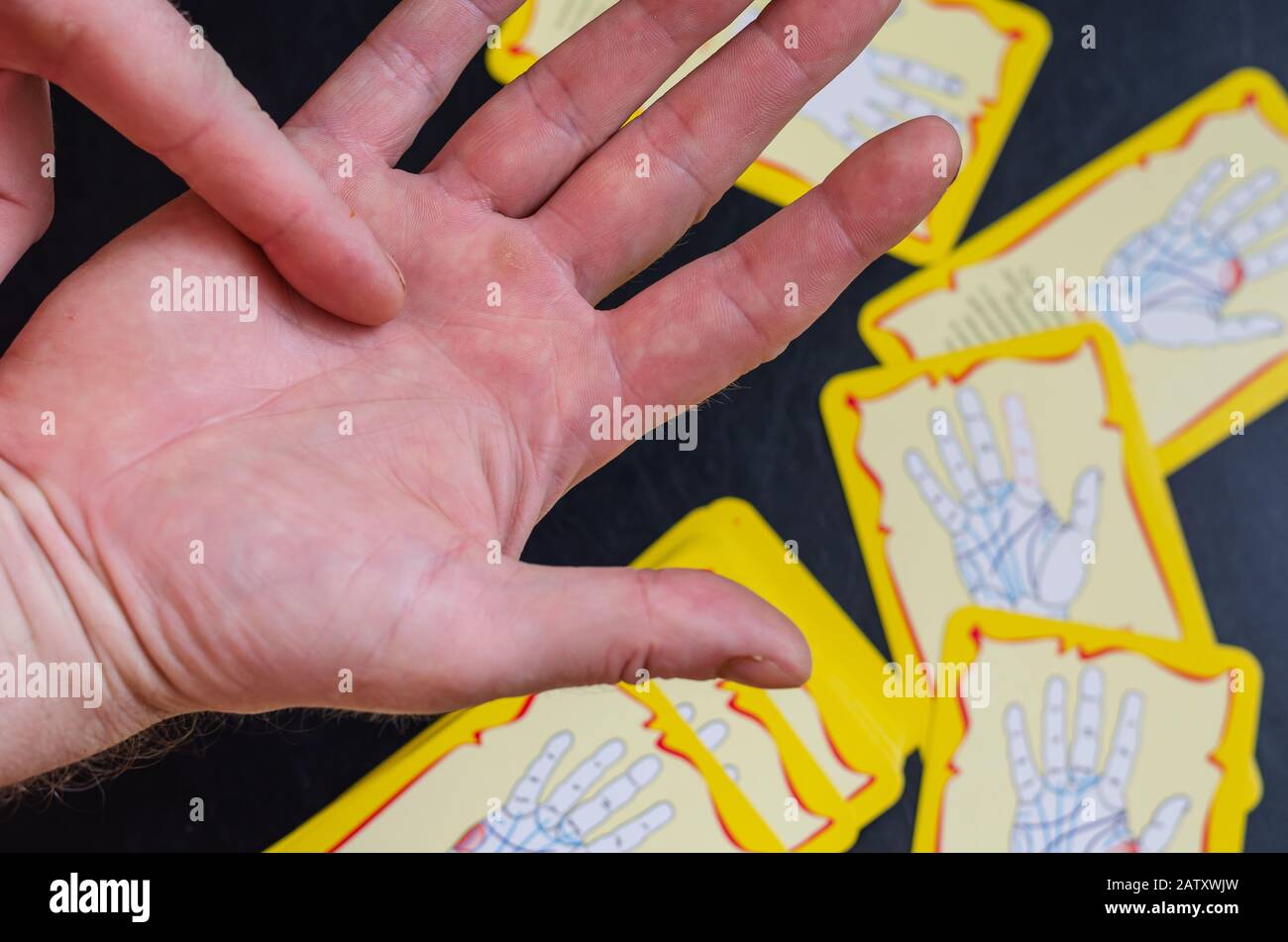 Chiromancer liest die Zeilen auf einer männlichen Hand. Rechte Hand über den Tisch. Auf dem Tisch sind Karten mit der Interpretation der Linien auf der Hand. Stockfoto