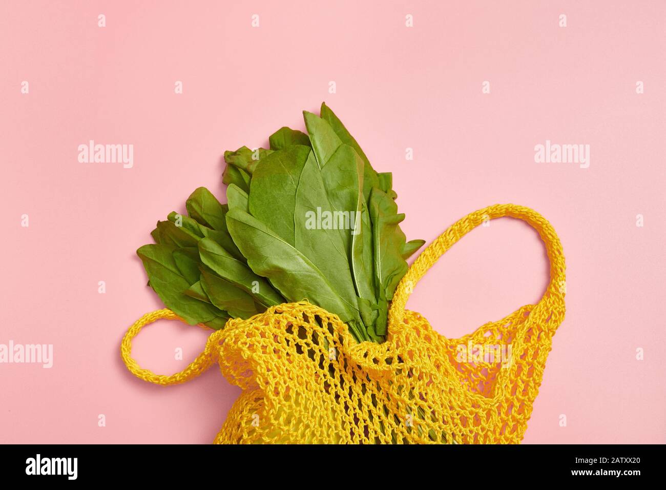 Grüne Sorrel in einem gelben Sack auf pinkfarbenem Hintergrund. Kein Abfall. Baumwolle Stockfoto